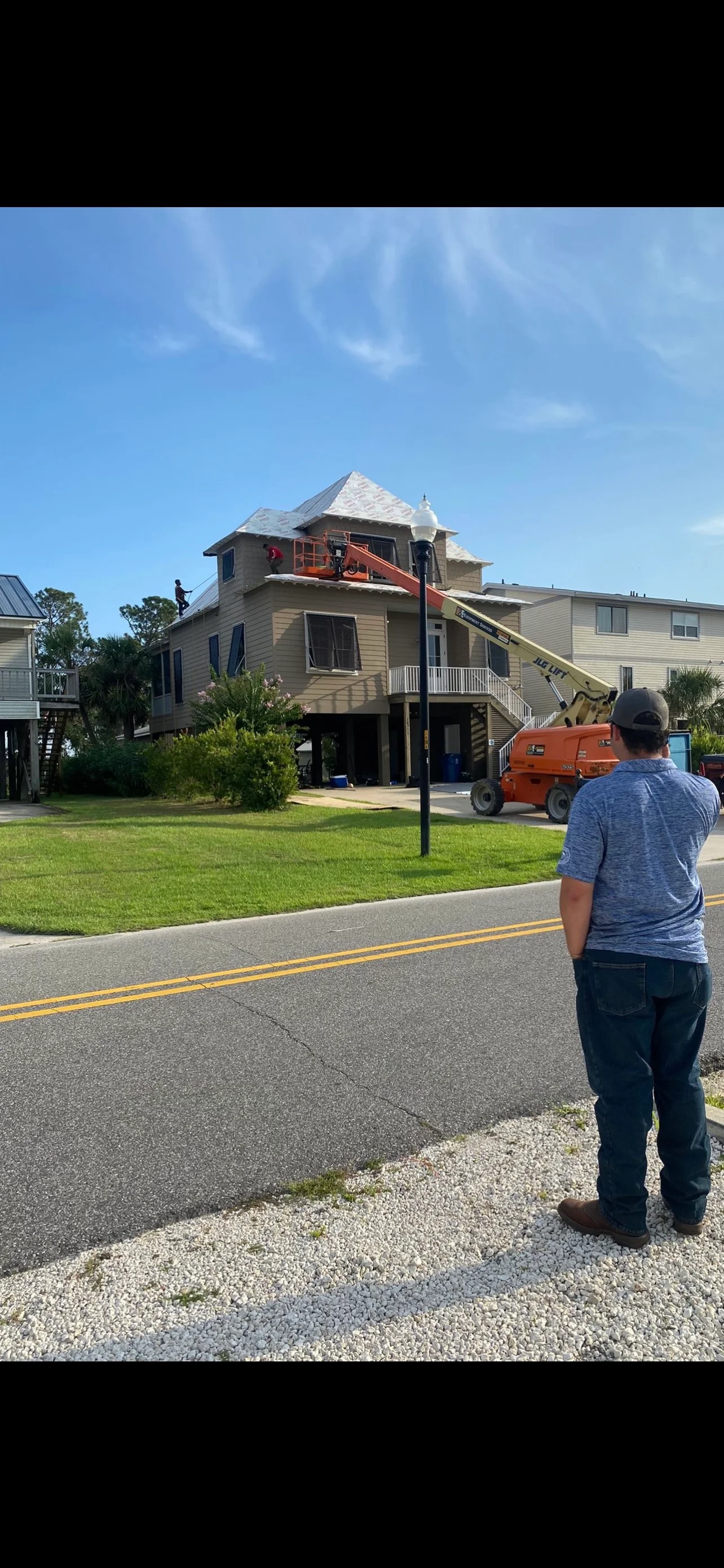 Elevated home with new asphalt shingle roof installation using aerial lift equipment