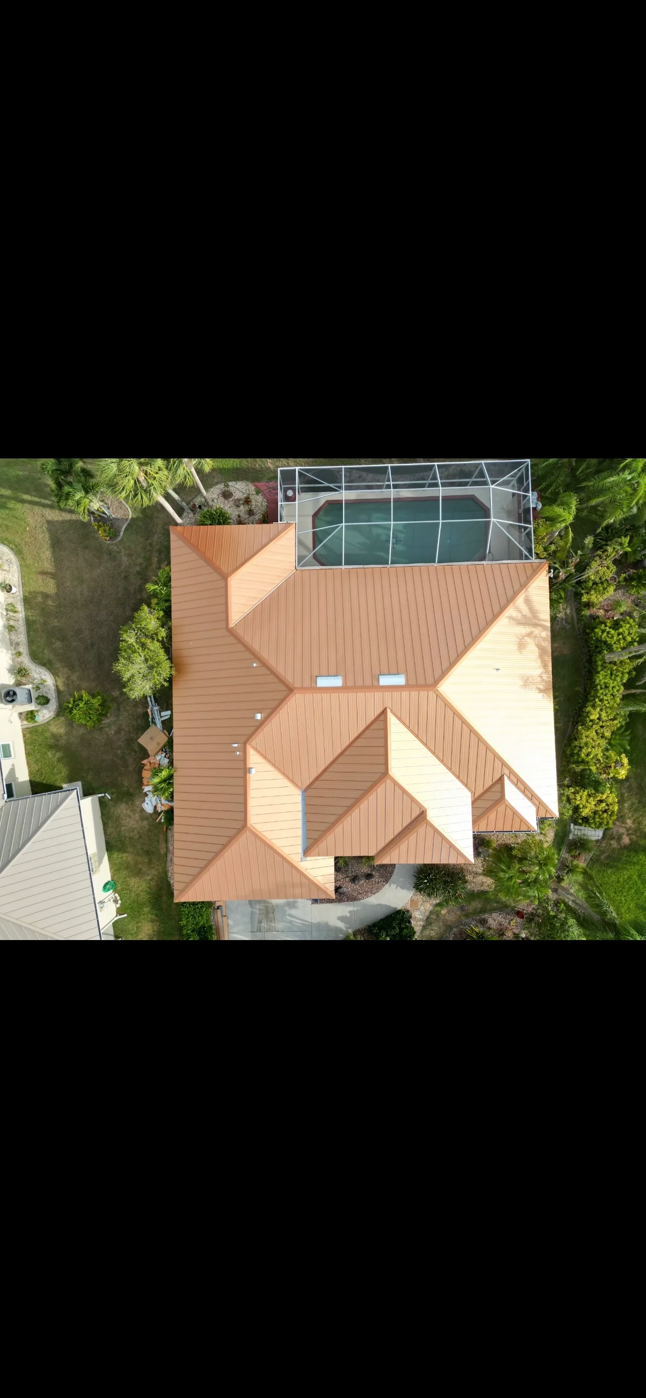Aerial view of copper-tone metal roof with standing seam panels and geometric design over residential home with pool enclosure