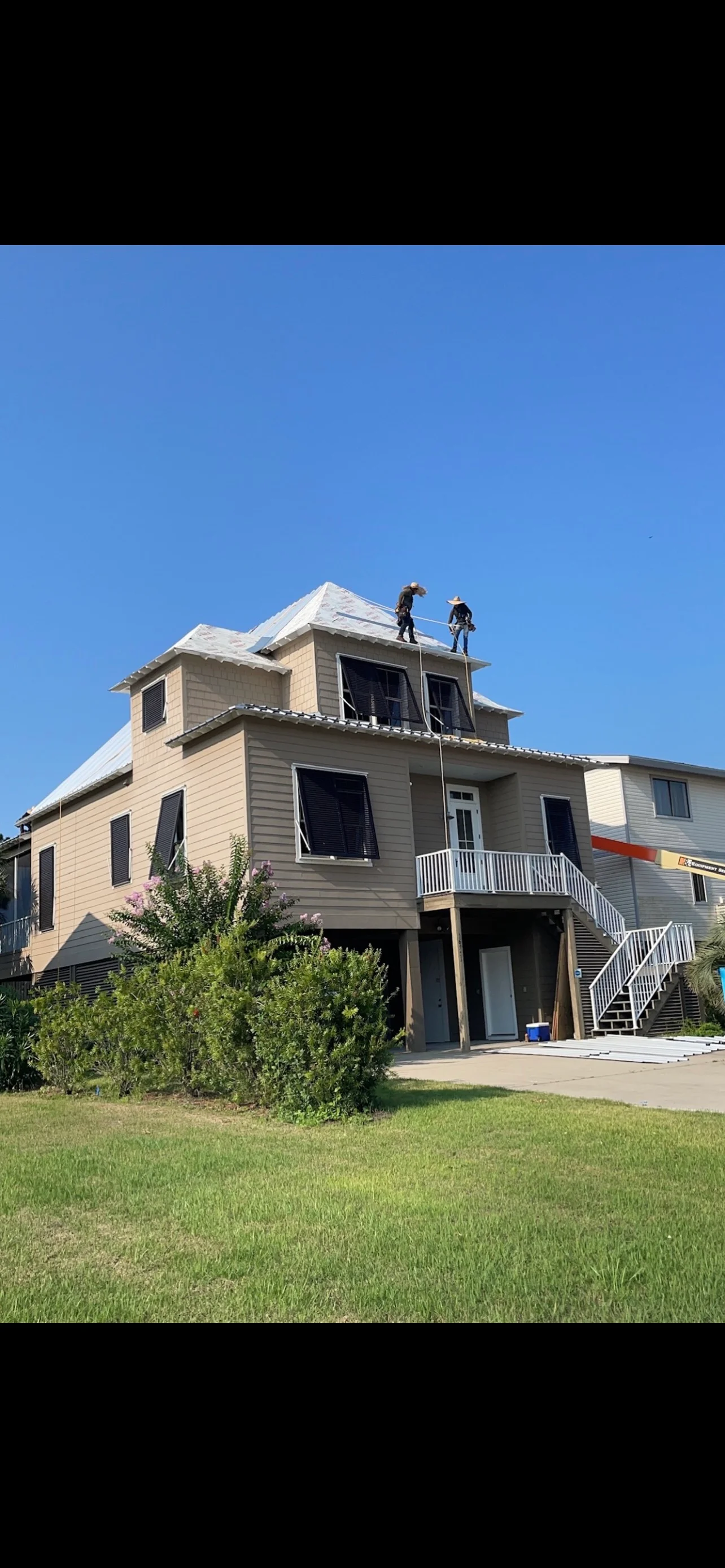 Two workers installing new asphalt shingles on residential roof with dormers and white trim