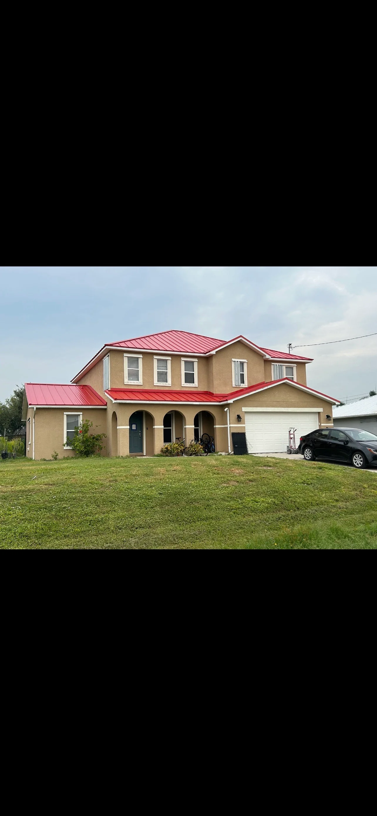 Red metal standing seam roof on tan two-story home with white trim and garage