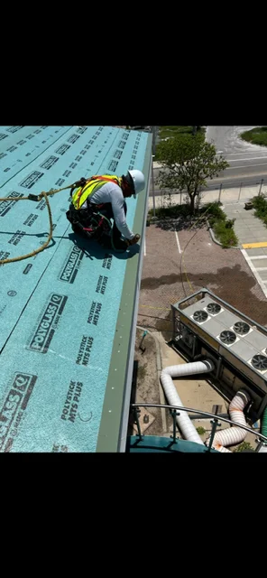 Worker installing blue synthetic roof underlayment on residential roof deck